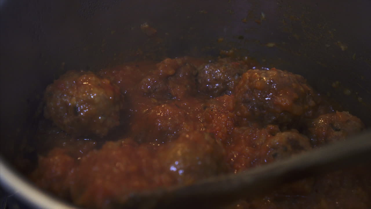 mano del chef revolviendo albóndigas recién preparadas en salsa de tomate