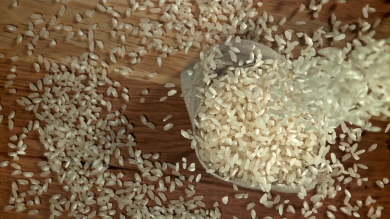 Witte rijstkorrels vallen in een klein zakje op een houten tafel