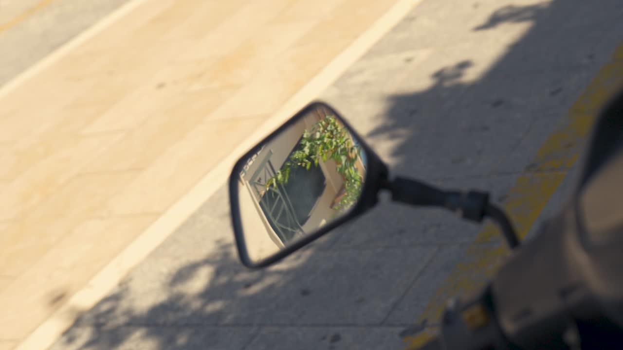 A slow motion moving shot of a moped's mirror reflecting the rooftops of the Greek street behind it