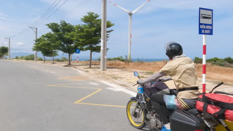 年轻男子骑着摩托车,带着冲浪板,风车,热带风景,沙<unk>