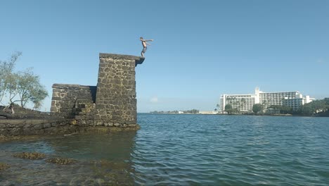 young man does a backflip from a stone-made dive platform into the ocean