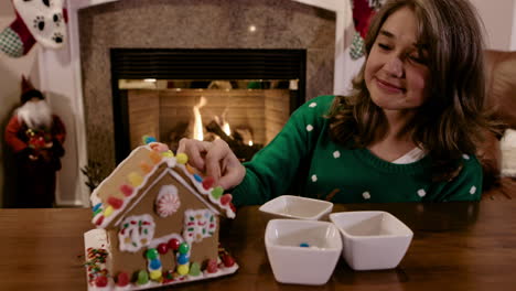 mujer atractiva decorando la casa de pan de jengibre de navidad