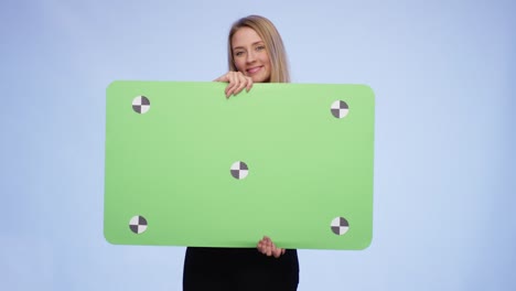 una joven alegre entrando en la imagen sosteniendo una tarjeta de pantalla verde de gran tamaño