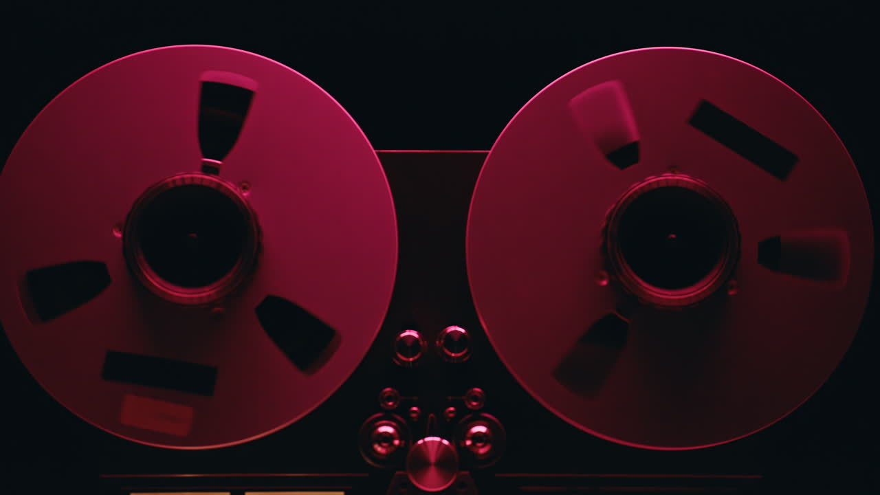 Analog reel spinning audio tape in neon red light closeup. Macro vintage machine