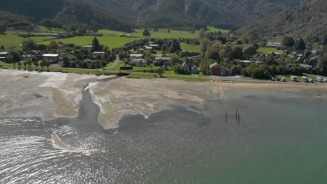 cámara lenta - volando sobre el agua del mar con la ciudad de anakiwa en el fondo, sonido de la reina charlotte, sonidos de marlborough, isla del sur, nueva zelanda - antena