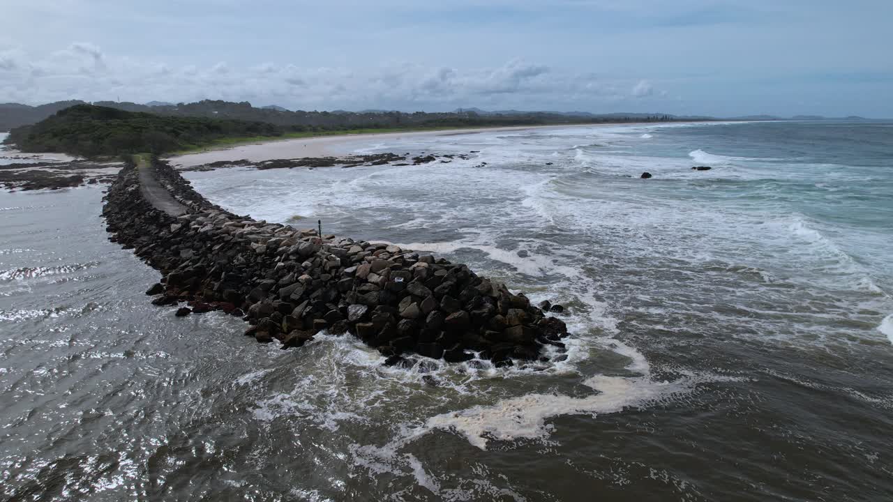 Rocky Seawall At The Mouth Of Brunswick River With Brunswick Heads Main Beach In Background. NSW, Australia. aerial orbiting shot