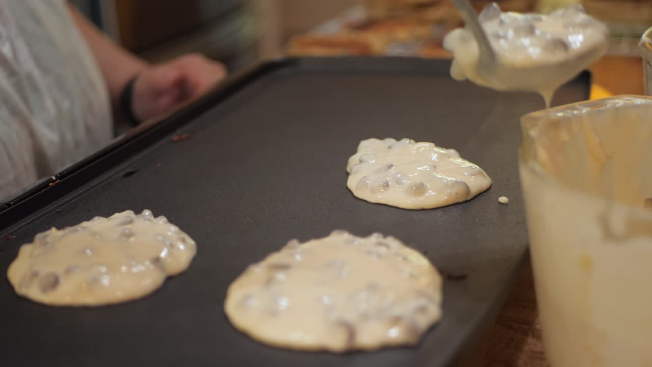 여자는 슬로우 모션으로 가열된 팬에 초콜릿 칩 팬케이크 반죽을 놓습니다.