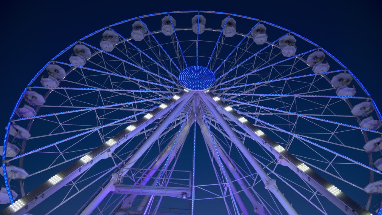 View of a white ferris wheel illuminated in the evening with the blue sky on the background