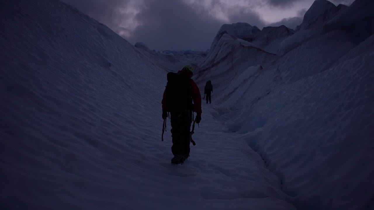 Clip of two men walking on a snowy mountaintop in  torres del paine national park, patagonia, chile, on a dark morning