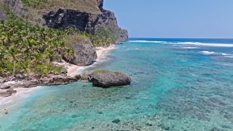 Slow-Aerial-flyover-crystal-clear-water-with-coral-reef-and-private-sandy-beach-along-coastline-during-summer-day