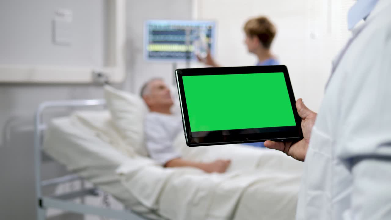 초록색 화면 태블릿을 들고 있는 의사는 배경에 흐릿한 환자 남성을 들고 있습니다.