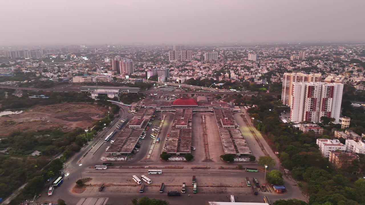 Aerial view of a large bus terminal in Koyembedu, Chennai Known as CMBT, with a sprawling cityscape and modern high-rises in the background, showcasing urban transportation and development