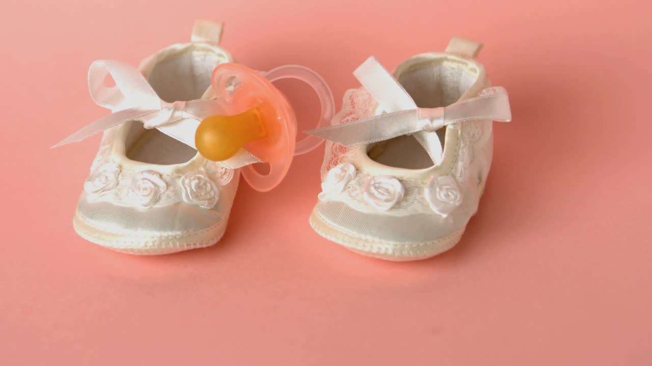 Pink soother falling onto baby shoes