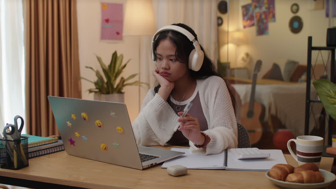 Pensive Schoolgirl Doing Homework on Laptop and Listening to Music