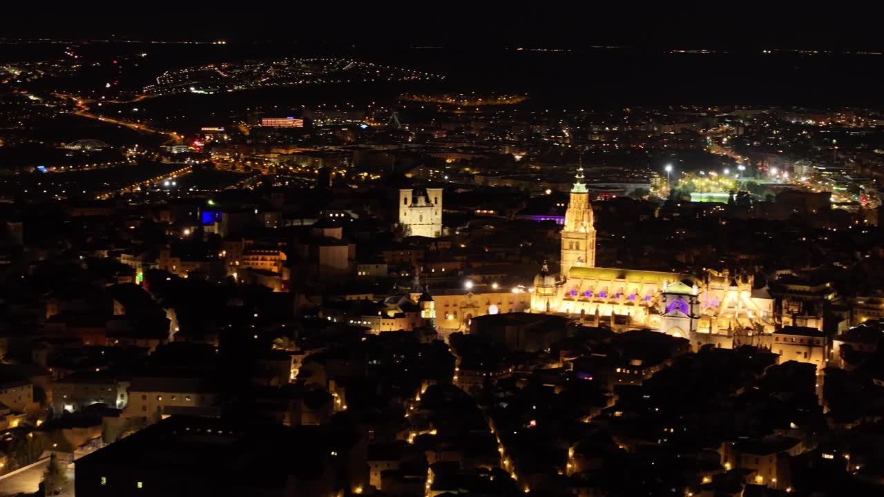 Flight in reverse with a drone filming in 70mm of the city of Toledo at night, we see the cathedral with spectacular lighting and the rest of the lights on the streets create that nocturnal magic