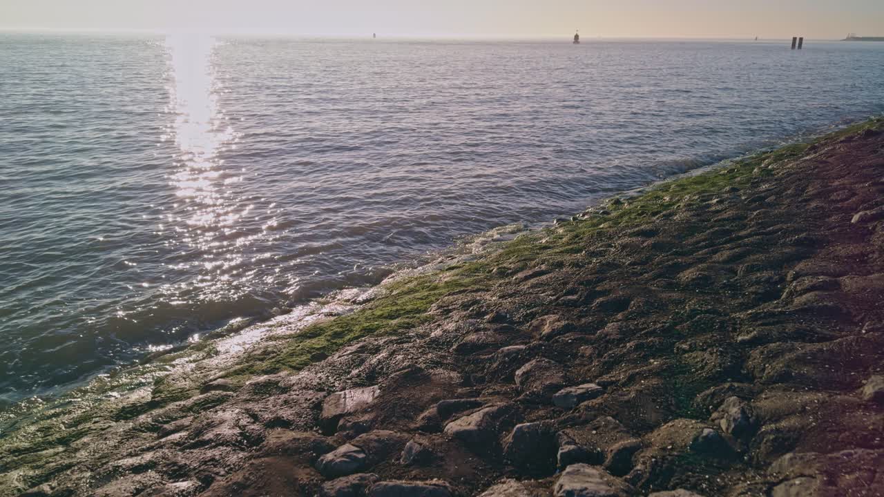 Vista da una spiaggia soleggiata verso il Mare del Nord in Europa, con onde marine e luce solare.