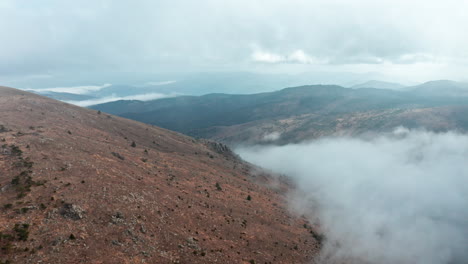 Misty-mountain-landscape-with-clouds-rolling-over-hills-at-dawn,-wide-shot