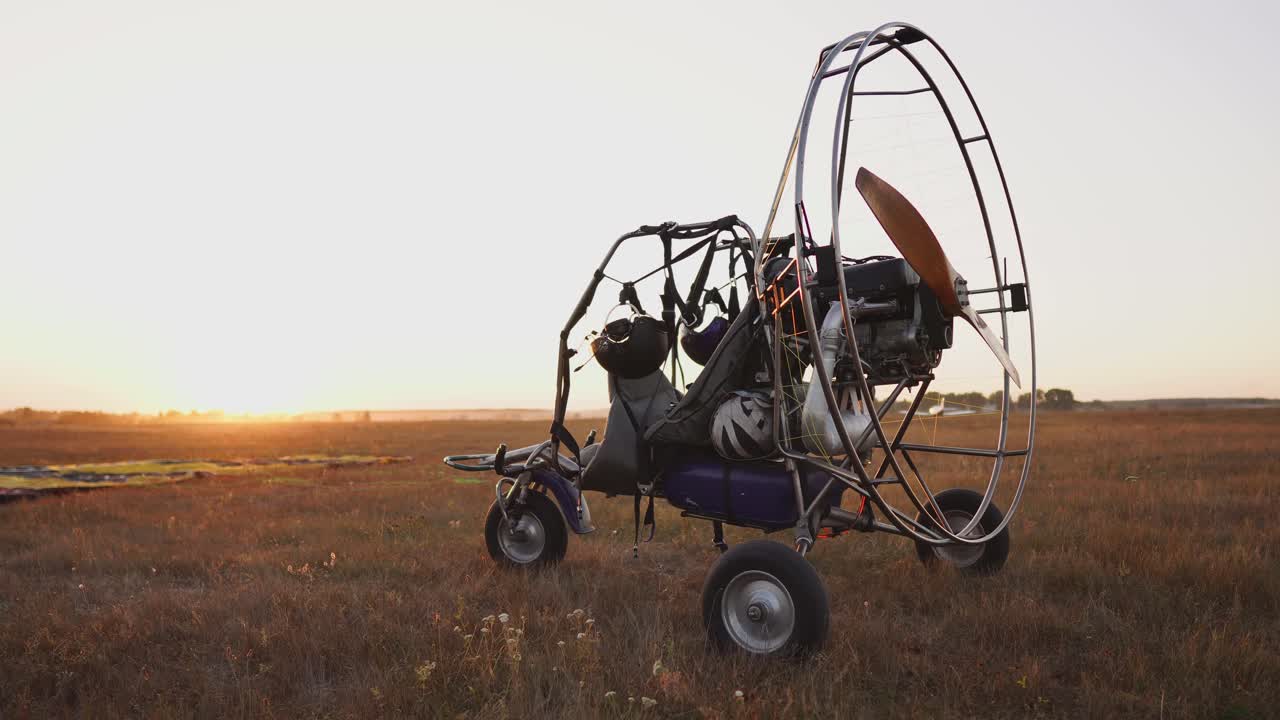 모터 패러글라이더는 해가 지는  ⁇ 빛 아래 공항에 서 있습니다. 배경에는 비행기가 이륙하고 낙하산 투수들이 앉습니다. 카메라가  ⁇ 도를 따라 움직입니다.