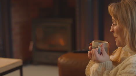 Woman-At-Home-In-Lounge-With-Cosy-Fire-With-Hot-Drink