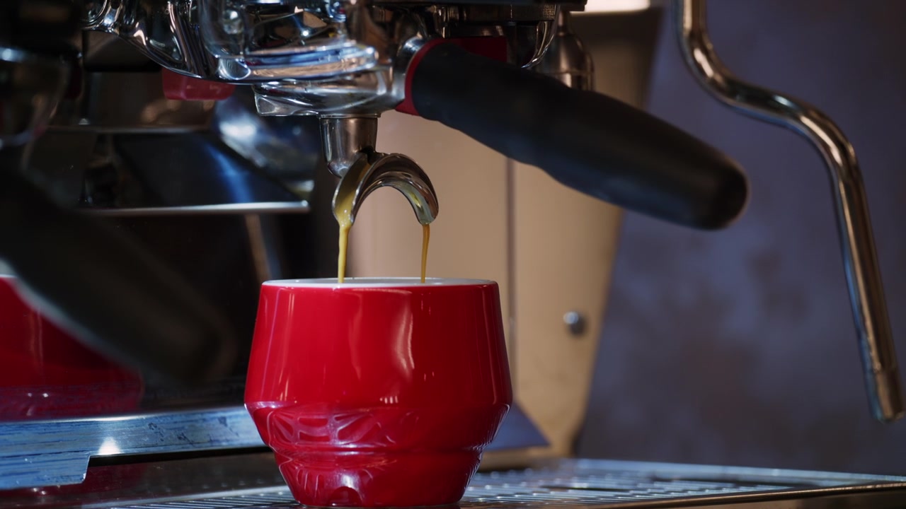 Expresso fresco fluindo de uma máquina de café profissional para uma xícara de cerâmica vermelha.