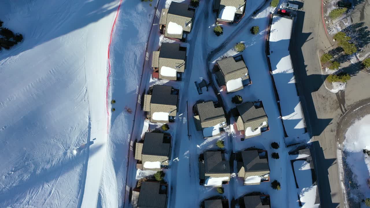 Big Sky, Montana, bird’s eye drone footage of cozy alpine condos blanketed in white, sitting beneath snow-covered trees and towering peaks in a peaceful and scenic winter mountain escape