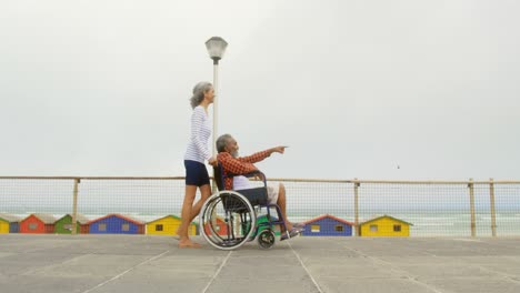 side view of active senior african american woman pushing disabled man in wheelchair on promenade 4k