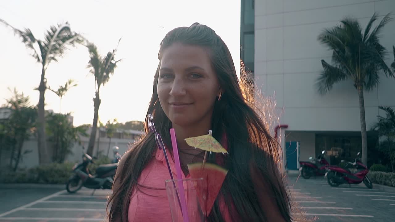 mujer sonriente con bebida de pie por el estacionamiento del scooter del hotel