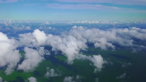 a beautiful scene of clouds and a forested coast as seen from the window of a plane in daylight