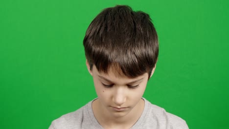 serious thinking curiosity teenager rising his head and looking at camera. calm, unhappy alone young boy over green chroma key background. close up kid portrait. 4 k video
