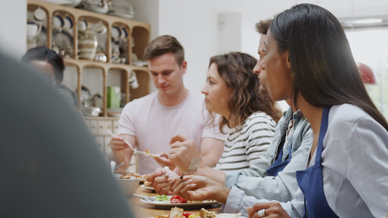 grupo de hombres y mujeres sentados alrededor de una mesa comiendo la comida que han preparado en la clase de cocina