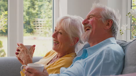 Pareja-De-Ancianos-Jubilados-Sentados-En-Un-Sofá-En-Casa-Tomando-Café-Y-Viendo-Televisión-Juntos