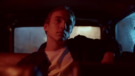 young man sitting in car backseat at night, looking around thoughtfully