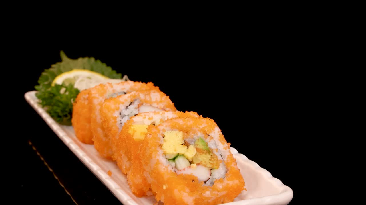 Un piatto rettangolare di sushi California roll ruota fluidamente su uno sfondo nero, illuminato da una morbida luce da studio, evidenziando colori vivaci e ingredienti freschi