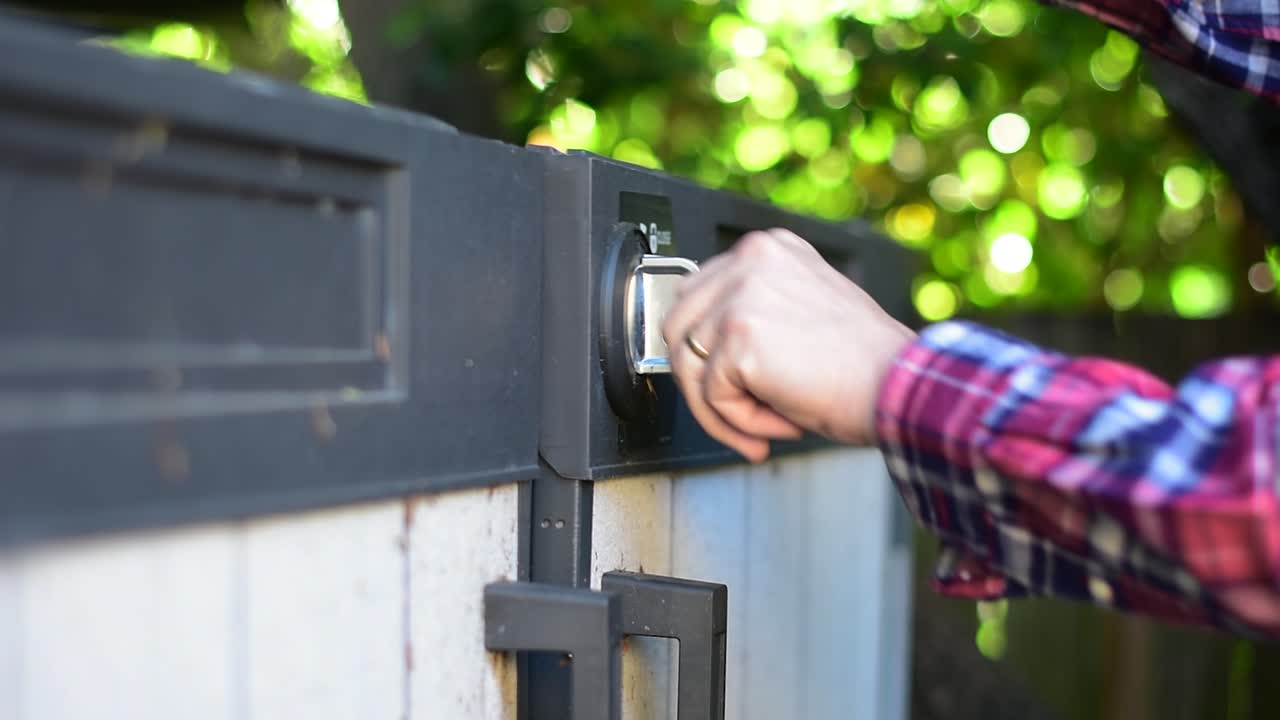 Beautifully shot close up of a padlock and latch on a shed with hands reaching in to use a key to unlock and remove the lock and open the lid and door of the shed, with stylish bokeh