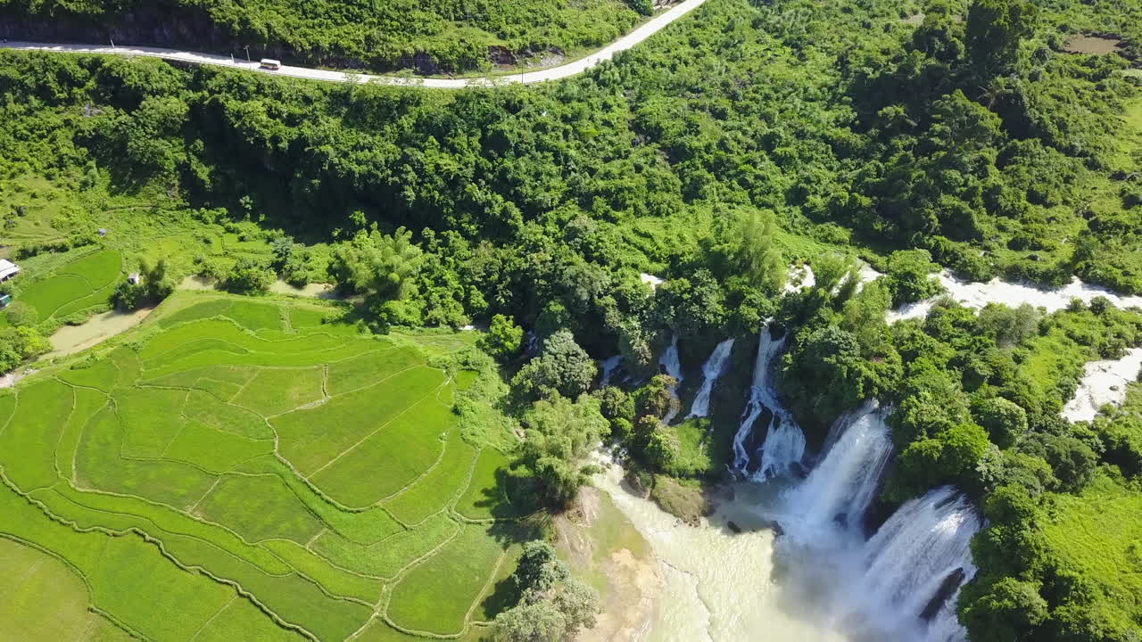 Vista aerea delle Cascate di Ban Gioc tra vegetazione lussureggiante e un fiume che scorre.