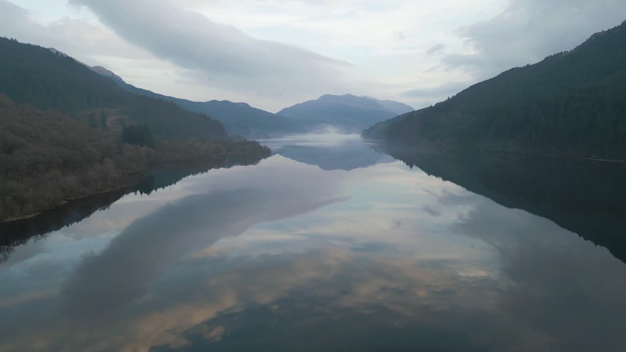 Reflections on Still Loch Waters Surrounded by Mountain Silhouettes