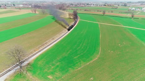 steam train puffing along amish farmland on a sunny summer day as seen by a drone