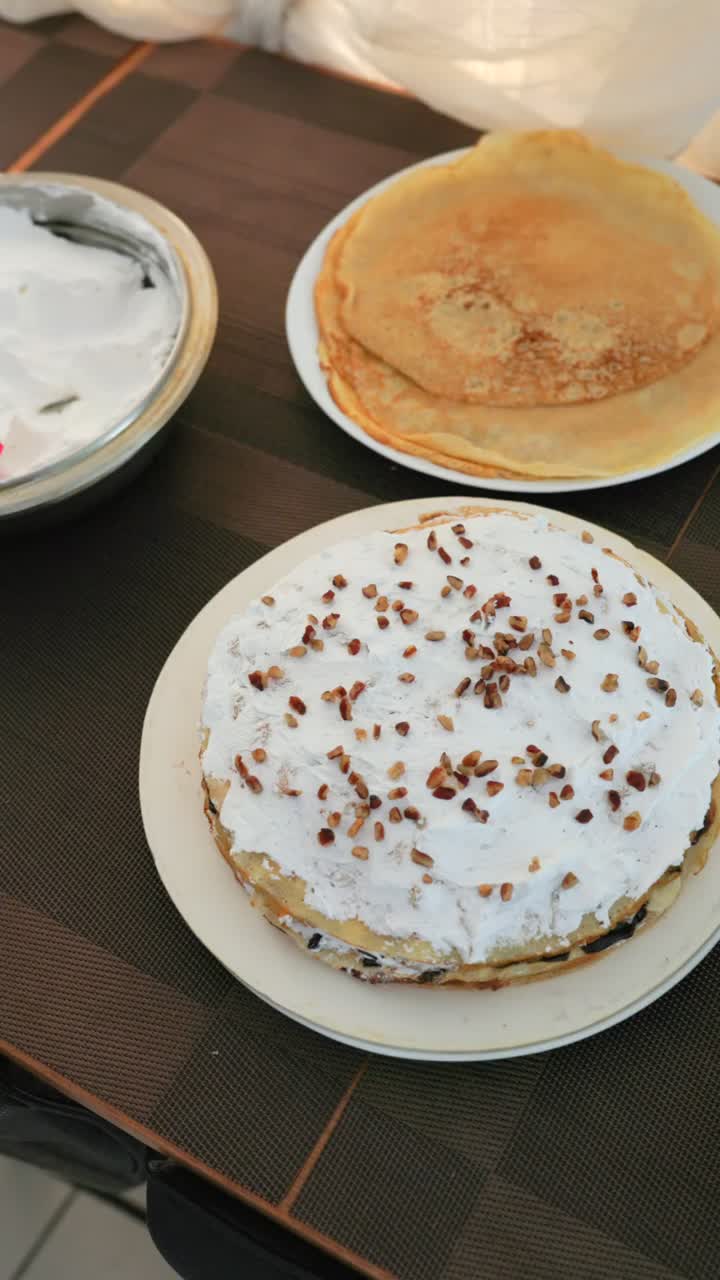 Crepe cake layer topped with whipped cream and sprinkled chopped nuts. Vertical close up