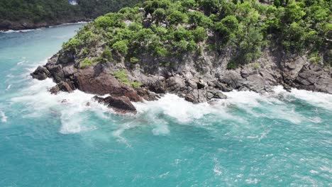 Tranquil-aerial-wide-shot-of-water-crashing-on-the-rocks-shore-sand-blue-sky-white-clouds-turquoise-water-relaxation-vacation-tourism-cliff-hill-mountain