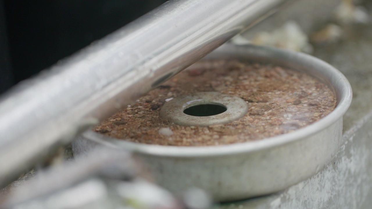 A circular metal component with orange brown corrosion and a central hole rests beside a diagonal steel pipe.
