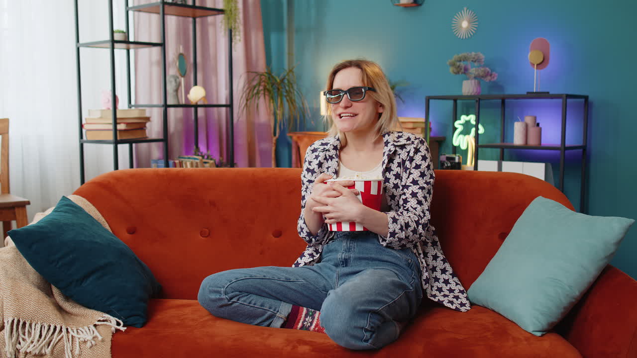 joven emocionada sentada en el sofá comiendo palomitas de maíz y viendo un interesante juego de serie de televisión