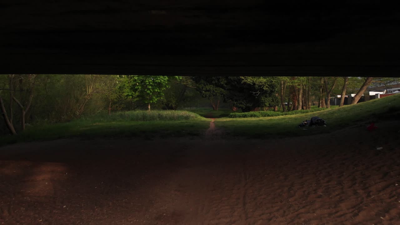 Slow low drone clip flying under a concrete bridge towards a narrow path in Thetford, England