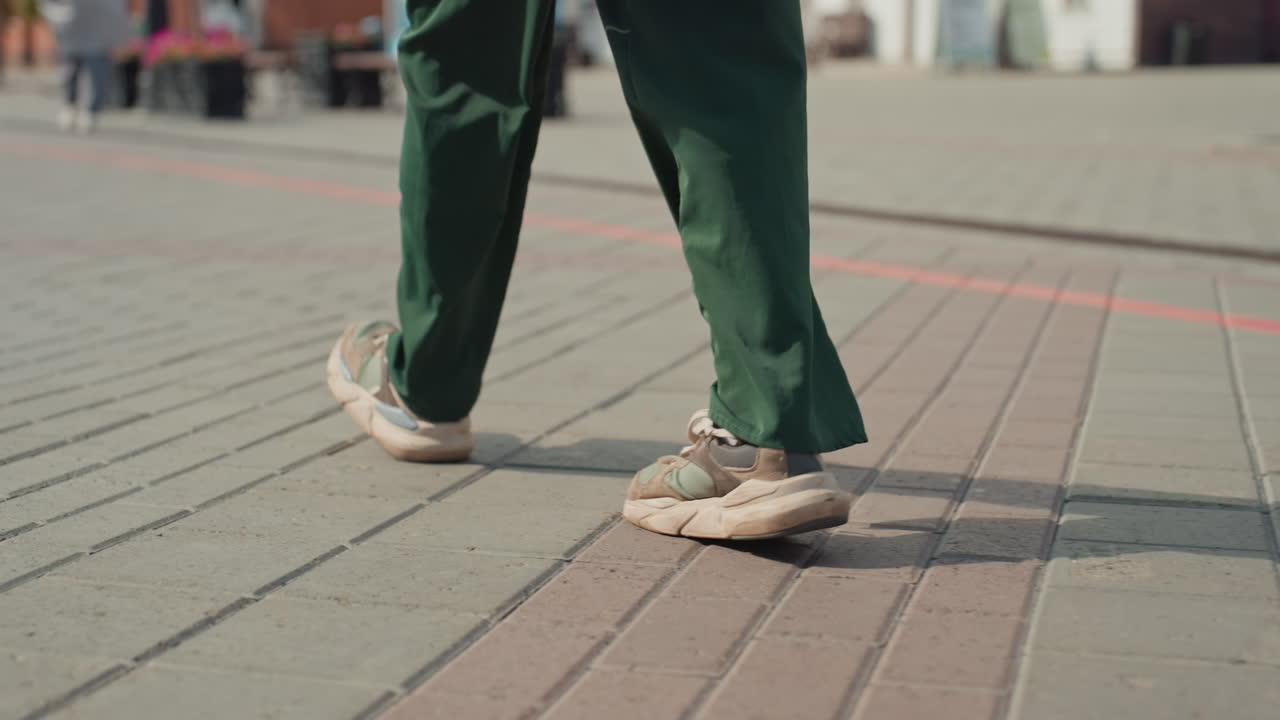 closeup sneakers on city pavement showing lowangle detail of feet and sole in green pants rhythmic steps create dynamic shadow and texture on patterned sidewalk style blogger commuter meeting
