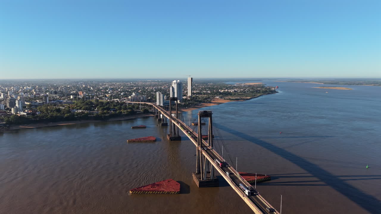 Forward drone descent looking south, highlighting the impressive length and magnitude of the General Belgrano Bridge with heavy morning traffic moving across it