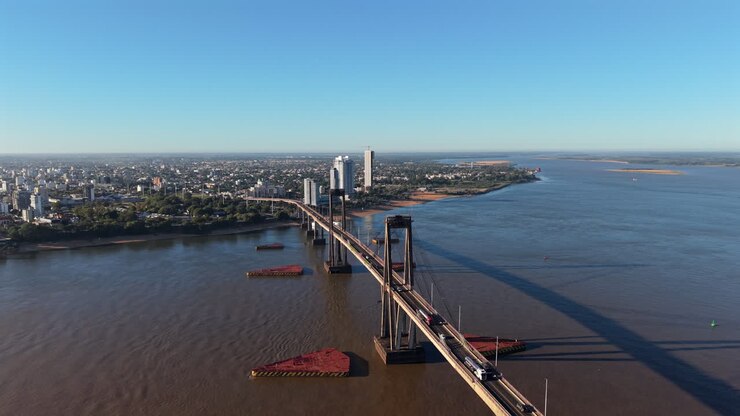 Discesa frontale di un drone con vista a sud, che mette in risalto l'imponenza e la lunghezza notevole del ponte General Belgrano con traffico mattutino intenso.