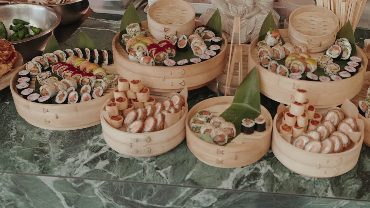 다양한 스시 롤을 여러 가지 속 재료와 함께 대나무 찜기에 담아 대리석 테이블에 놓은 모습