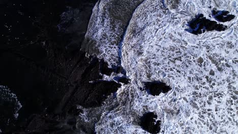 drone bird's eye pull out of low tide waves and rock formations at mavericks beach, california