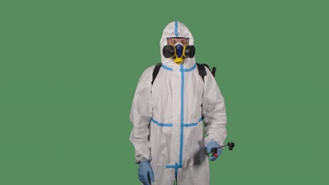 man wearing personal protective suit, safety glasses, a respirator and gloves disinfects and decontaminats infected area on a green screen, chroma key. close up. slow motion