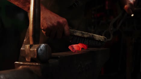 mid-section of blacksmith using wire brush on hot iron