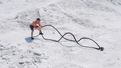 male bodybuilder doing intense athletic exercises with ropes. training on the nature on white sand